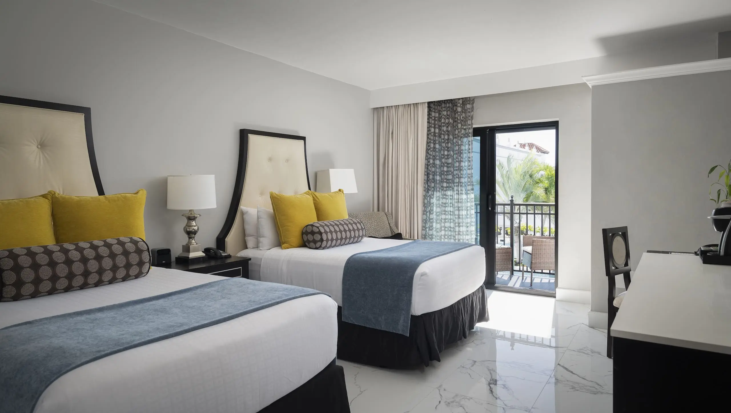 Inn on Fifth guest room with two king beds, charcoal throw and yellow pillow, and sliding doors opening to a balcony