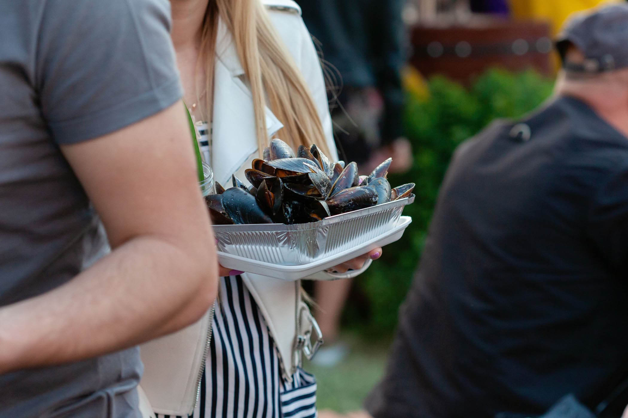 A woman carrying a container of cooked mussels.